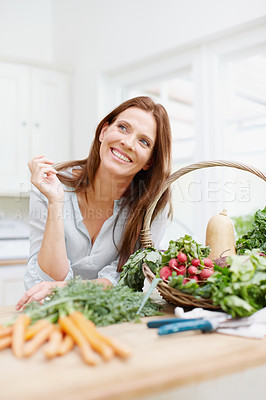 Buy stock photo A beautiful woman leaning on a kitchen counter next to a basket of vegetables