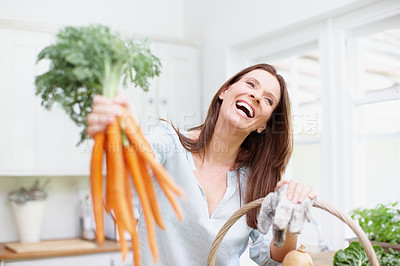 Buy stock photo A beautiful brunette holds up a bunch of carrots in her kitchen as she laughs