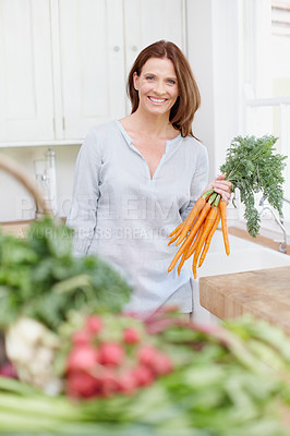 Buy stock photo A beautiful woman stands in her kitchen while holding a bunch of carrots