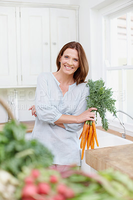 Buy stock photo A beautiful brunette holds a bunch of carrots while standing in her kitchen 