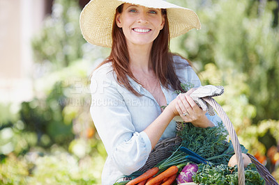 Buy stock photo A gorgeous woman in a straw hat holding a basket of fresh vegetables in her garden