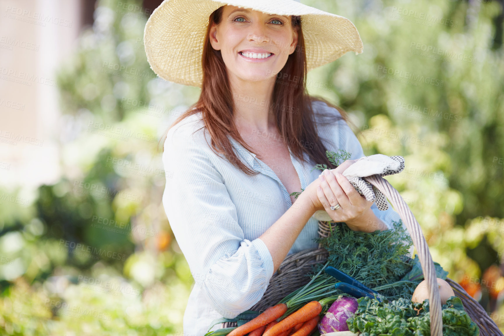 Buy stock photo A gorgeous woman in a straw hat holding a basket of fresh vegetables in her garden