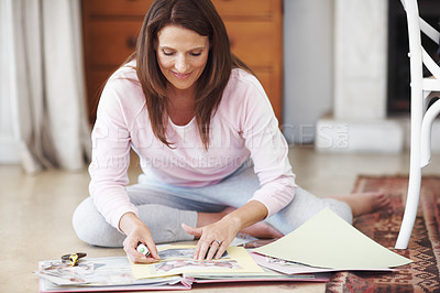 Buy stock photo An attractive woman working on a scrapbook while sitting on the floor indoors
