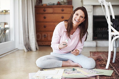 Buy stock photo A smiling woman working on a scrapbook while sitting on the floor in a home interior