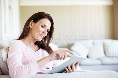 Buy stock photo An attractive woman using a digital tablet while sitting on a sofa