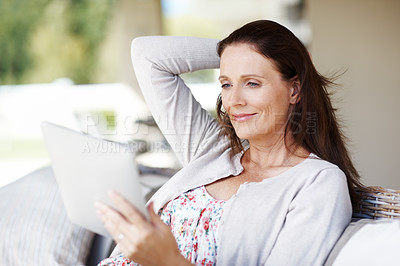 Buy stock photo An attractive woman reading something on her e-reader while sitting outdoors