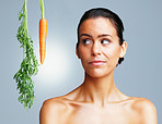 Topless young woman looking at carrot against colored background
