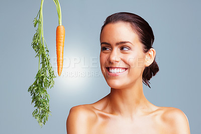 Buy stock photo Portrait of a cheerful young female looking at carrot against colored background