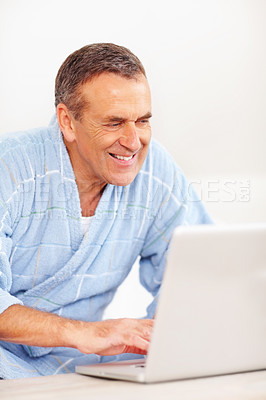 Buy stock photo Bathrobe, morning and mature happy man on laptop for email, social media or streaming subscription on sofa. Internet search, couch and senior person on computer, website or networking in living room.