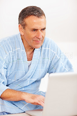 Buy stock photo Bathrobe, relax and mature man on laptop, checking email, social media or streaming subscription on sofa. Internet website, couch and senior person on computer, morning and networking in living room.