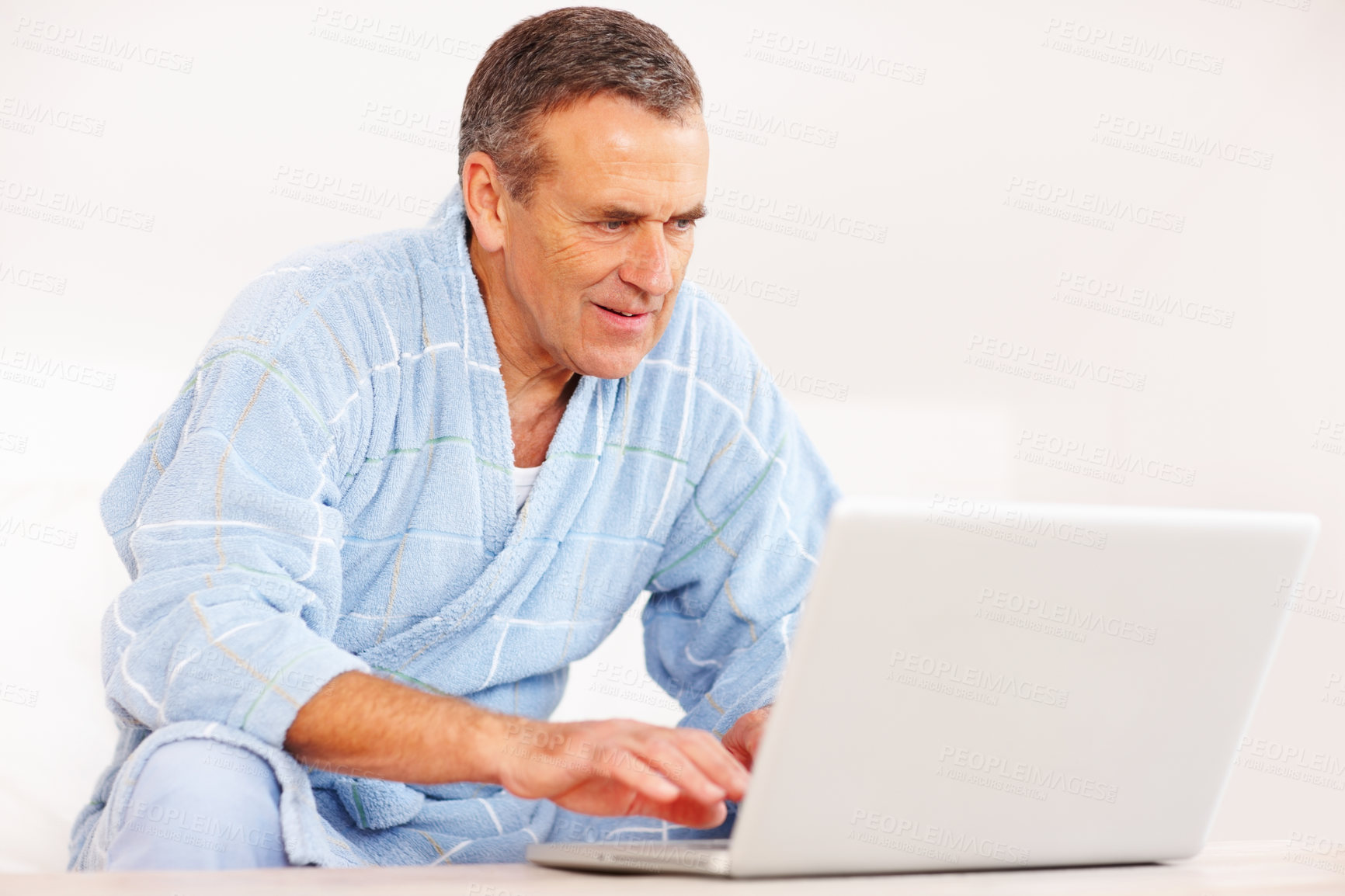 Buy stock photo Bathrobe, morning and mature happy man on computer for email, social media or streaming subscription on sofa. Internet search, couch and senior person on laptop, website or networking in living room.