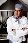 Mature chef with hands folded standing in front of vent hood