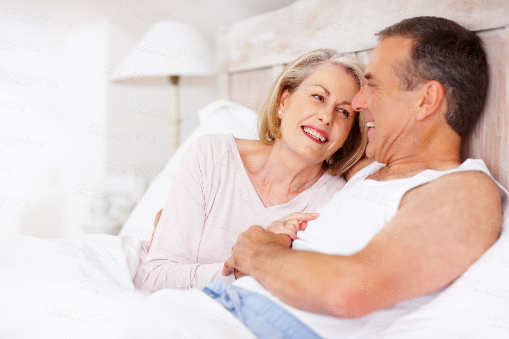 Buy stock photo Mature couple, smile and holding hands in bed for relax, love and retirement together with trust and care. Man, woman and cuddle in home bedroom for marriage, loyalty or break on weekend with support