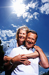 Mature man giving piggyback ride to wife against cloudy sky