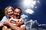 Senior woman hugging husband from behind against cloudy sky