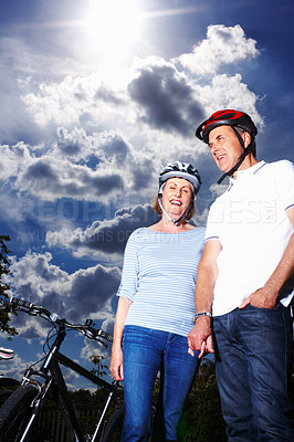 Buy stock photo Low section of romantic senior couple standing by bicycle against cloudy sky