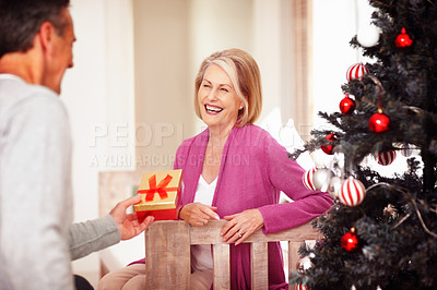 Buy stock photo Senior, happy couple and christmas with gift for surprise, offer or festive celebration at home. Mature man and woman with smile for present, ribbon box or tree on December holiday together at house