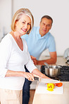 Smiling senior woman preparing food with man in background