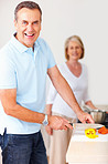 Cheerful senior man cutting vegetables and woman in background