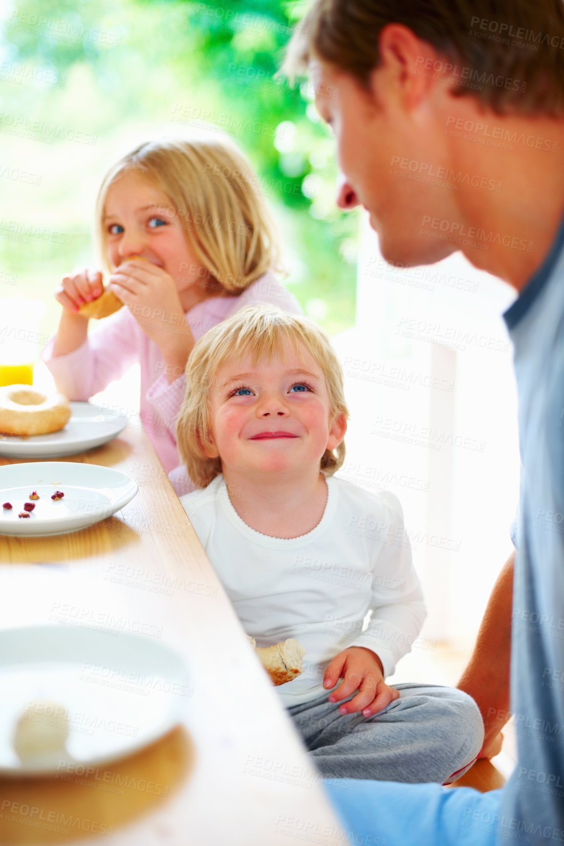 Buy stock photo Family, morning and eating breakfast before school, looking and hungry for nutrition, meal and doughnut. Father, children and enjoying food together for hunger, health and energy for good day