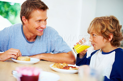 Buy stock photo Happy family, morning and breakfast on weekend, looking and eating for nutrition, orange juice and donut. Father, child and enjoying food together for hunger, health and energy for good day
