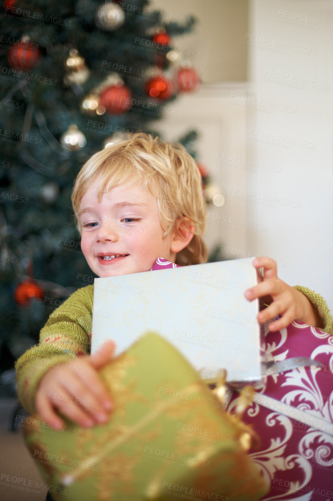 Buy stock photo Christmas, festive and a boy opening a present under a tree in the morning for celebration or tradition. Kids, gift and excitement with an adorable young child in the living room of his home