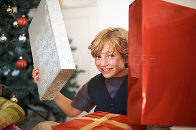 Buy stock photo Portrait, christmas and a boy opening a present under a tree in the morning for celebration or tradition. Kids, gift and excitement with a happy, young or cute child in the living room of his home