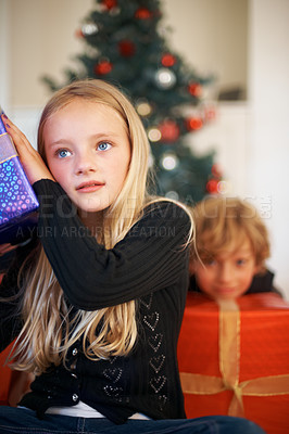 Buy stock photo Christmas, listening and a girl opening a present under a tree in the morning for celebration or tradition. Kids, gift and festive with an adorable young child in the living room of her home