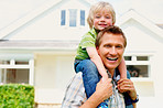 Mature man carrying his son on shoulder in front of house