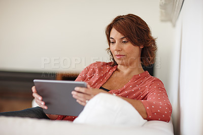 Buy stock photo Shot of a mature woman using a digital tablet on the sofa at home