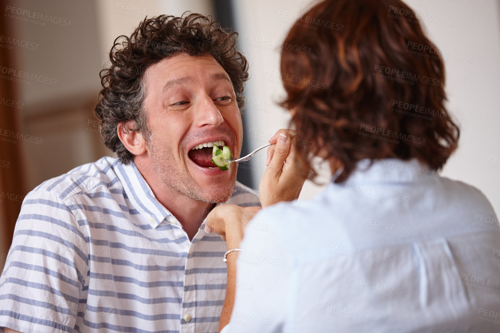 Buy stock photo Shot of a happy wife giving her husband a taste of food