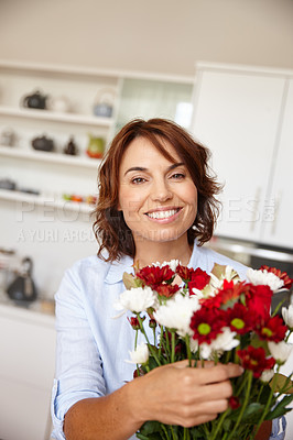Buy stock photo Shot of a mature woman adjusting flowers in a vase at home