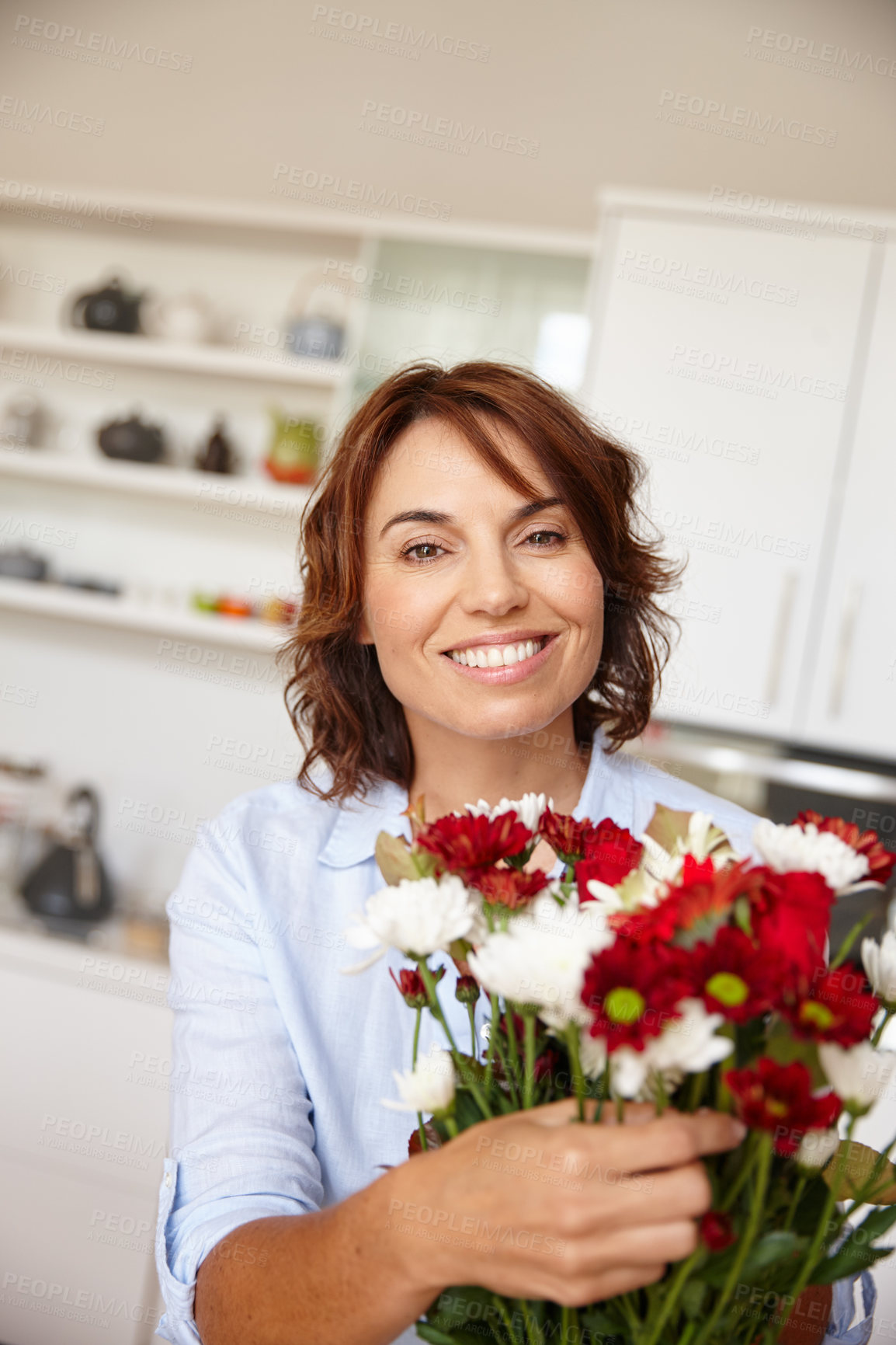 Buy stock photo Shot of a mature woman adjusting flowers in a vase at home