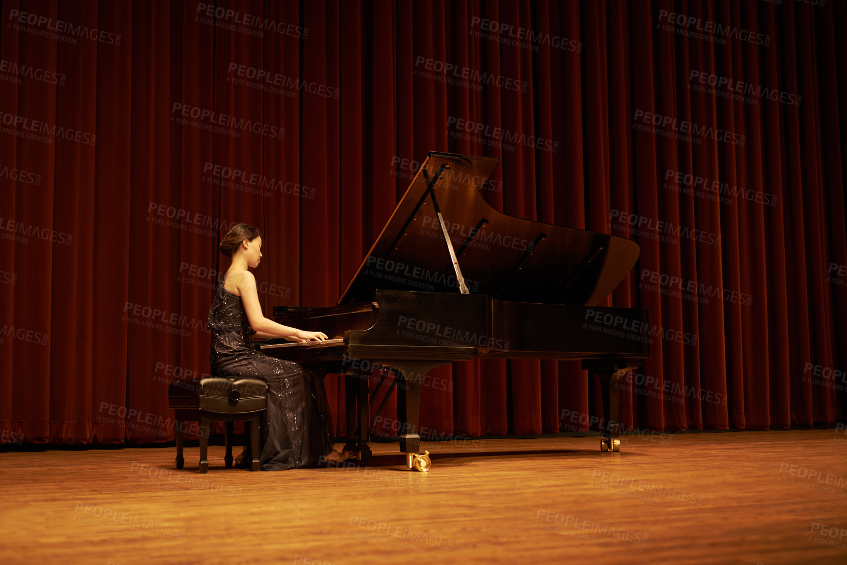 Buy stock photo Shot of a young woman playing the piano during a musical concert