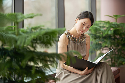 Buy stock photo Reading, plants and woman in home with book to relax with glamour, comfort and elegant fashion. Eco, green decor and Asian girl in house with files, reference and cool carbon neutral interior design