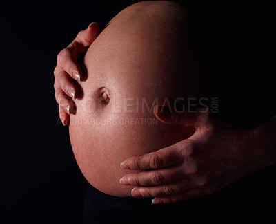 Buy stock photo Detail shot of a pregnant woman holding exposed belly against black background