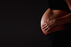 Pregnant woman feeling her baby against black - copyspace