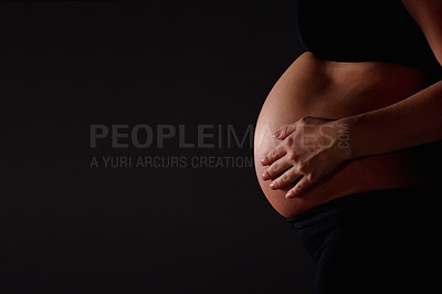 Buy stock photo Mid section of a pregnant woman feeling her baby against black background - copyspace