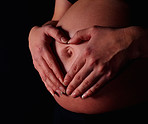 Pregnant woman making heart shape with hands against black