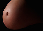 Detail shot of a pregnant woman's belly against black