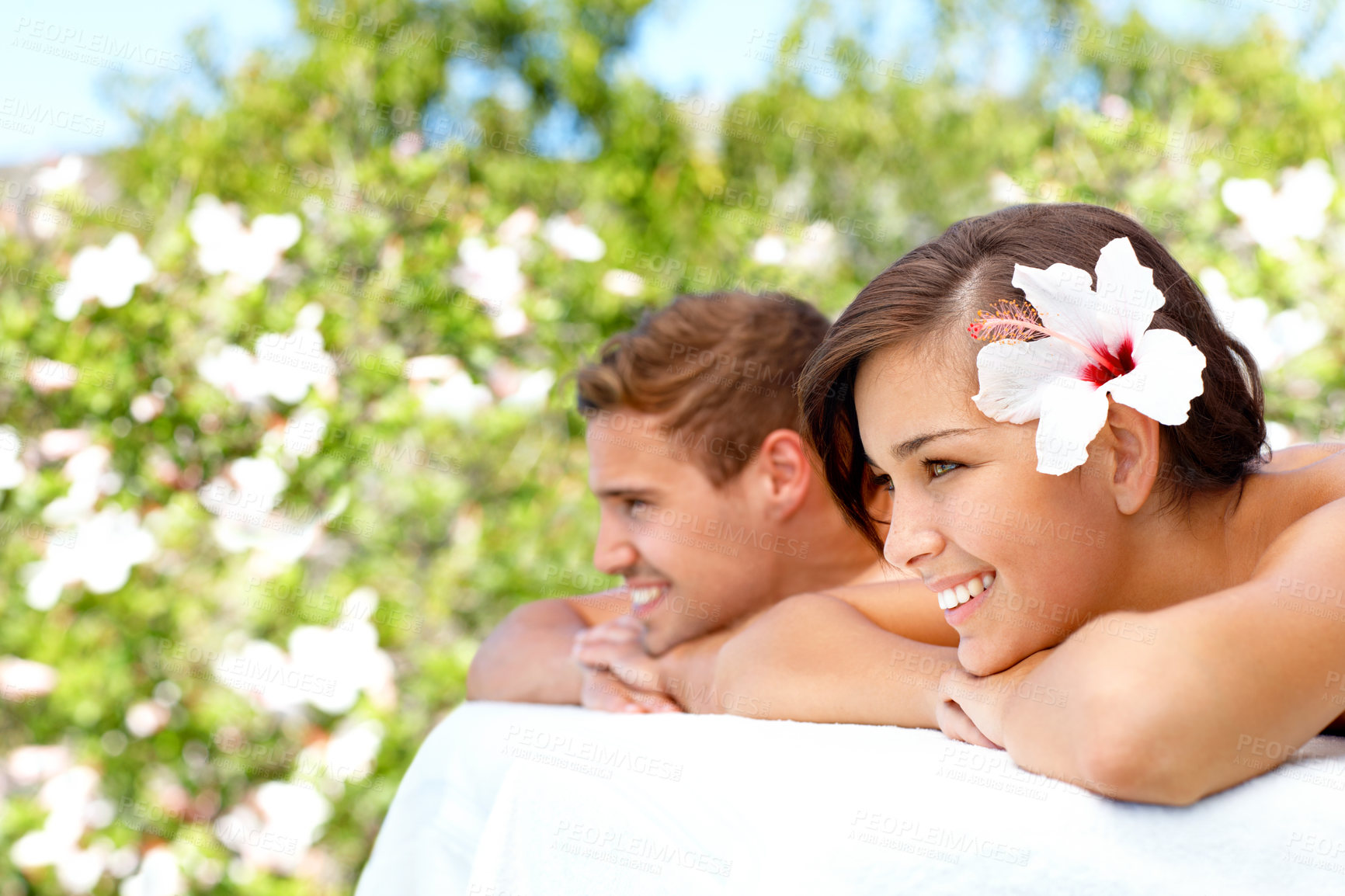 Buy stock photo Massage, relax and happy couple at outdoor spa for skincare, health or wellness on table. Smile, man and woman at luxury salon with hibiscus flower in nature for therapy on romantic holiday together