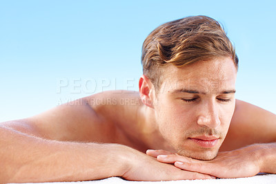 Buy stock photo Closeup face of a man feeling relaxed while lying against a blue sky background with copyspace. Carefree handsome young male dreaming and sunbathing while enjoying a spa day on a massage bed outside