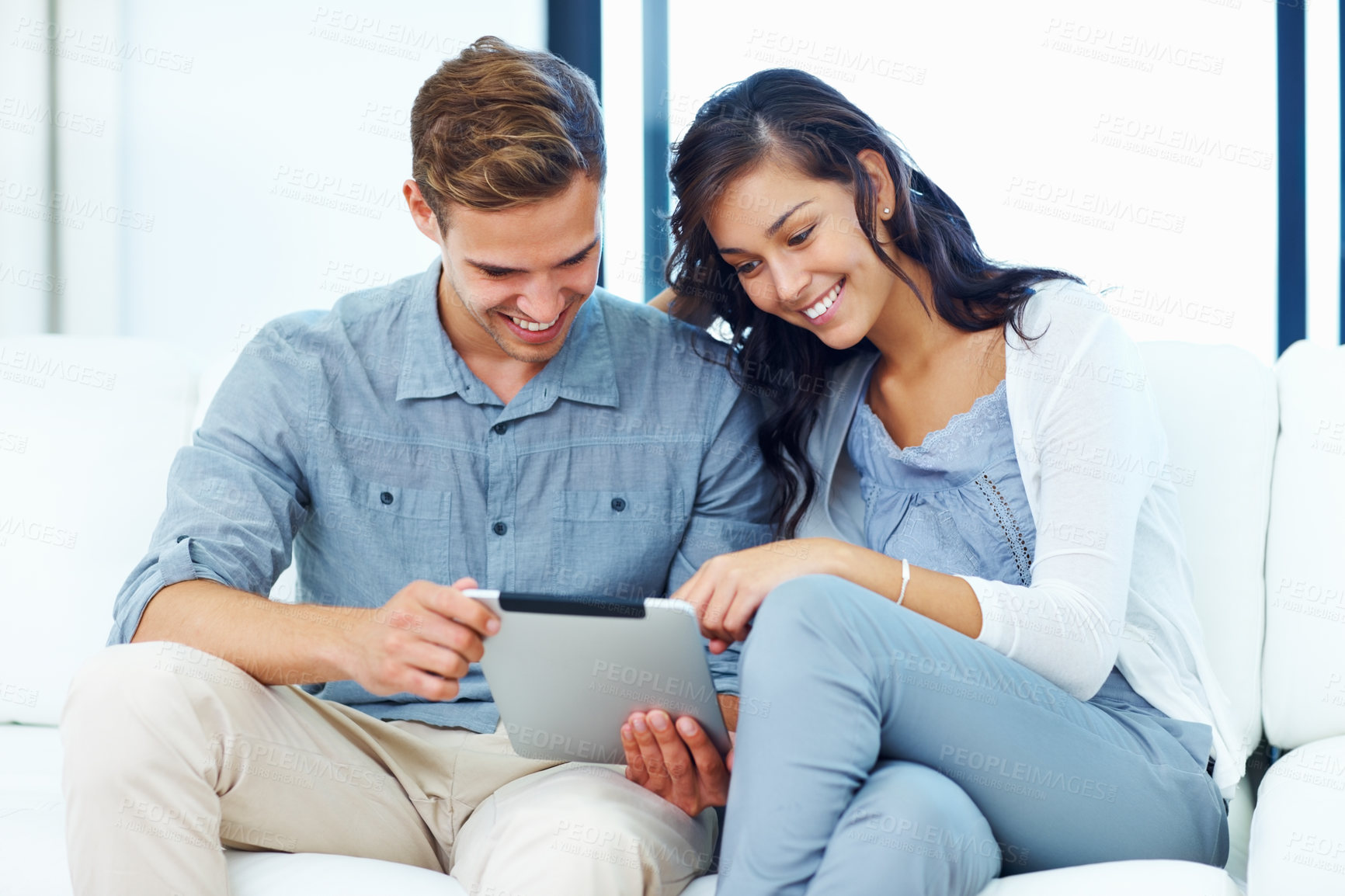 Buy stock photo Happy young couple on sofa smiling while using tablet PC