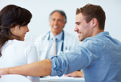 Buy stock photo Portrait of happy young couple smiling with mature doctor in background
