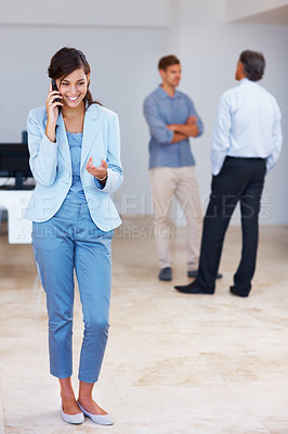 Buy stock photo Full length of happy business woman speaking on cellphone with colleagues in background