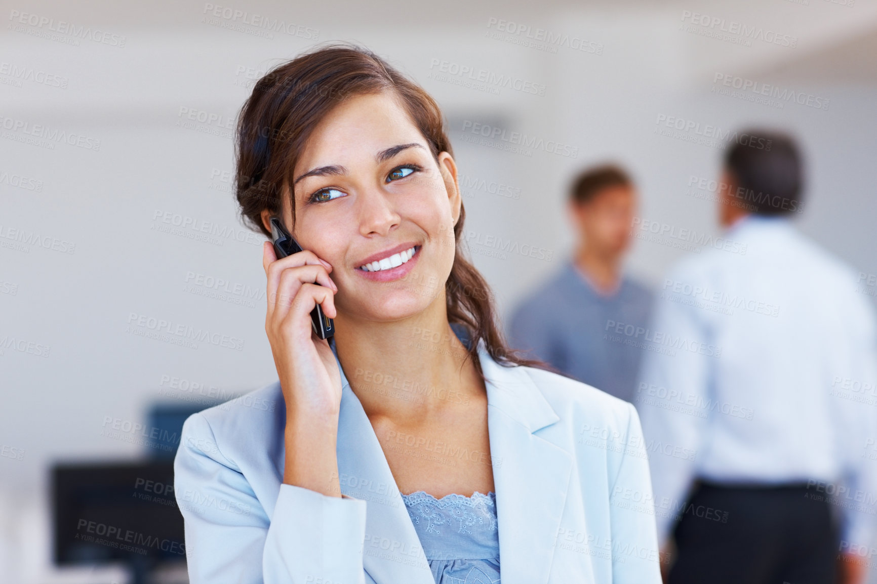 Buy stock photo Closeup of young female executive speaking on mobile phone with staff in background