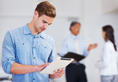 Buy stock photo Portrait of young business man working on electronic tablet with colleagues in background