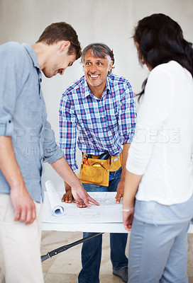 Buy stock photo Young couple reviewing blueprint with male contractor for home renovation