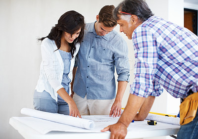 Buy stock photo Young couple examining blueprint while discussing house plans with architect