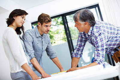 Buy stock photo Young couple discussing home plan on blueprint with architect